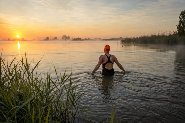 Adult swimmer wading into cold open water in Amsterdam, managing cold water shock by entering slowly and controlling their breathing.